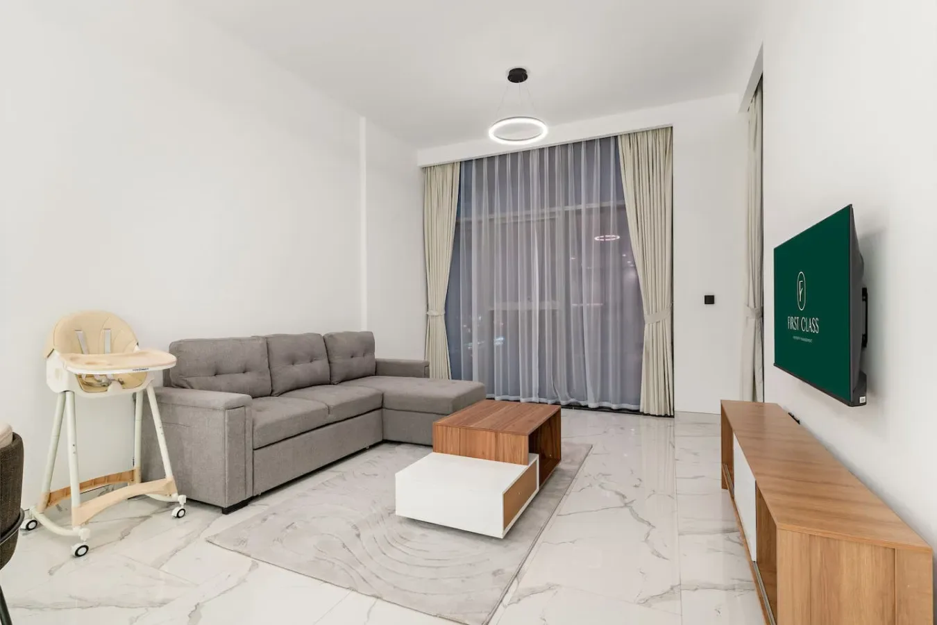 Una sala luminosa tiene un sofá seccional gris, mesas de centro y ventanas con cortinas largas.