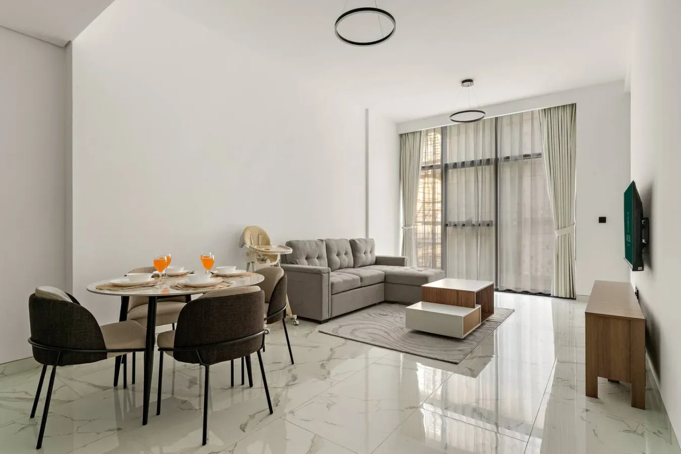 Una luminosa sala de estar y comedor con sofá, mesa de comedor y grandes ventanas con cortinas.