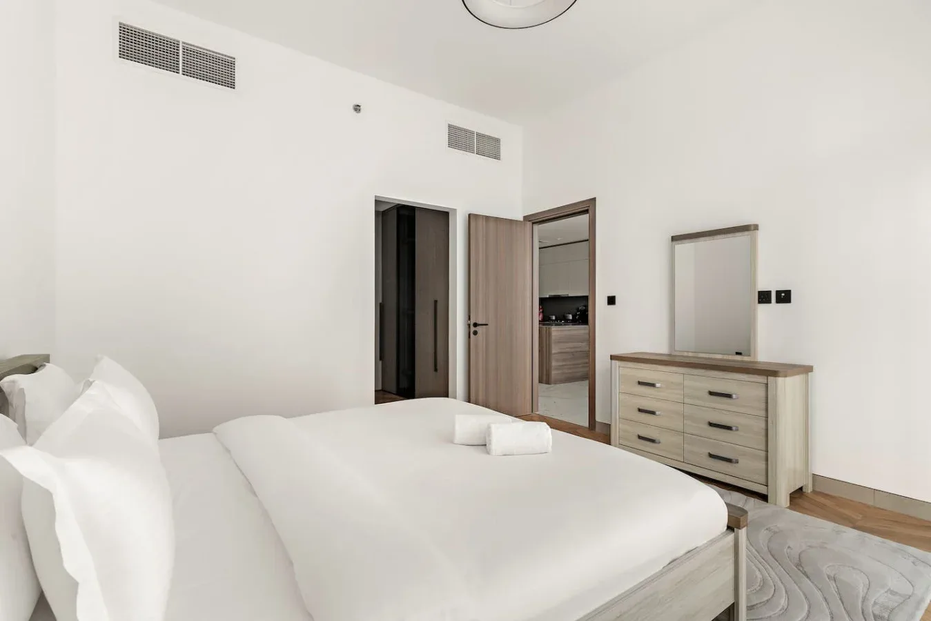 Un dormitorio luminoso con cama, cómoda y puerta abierta.