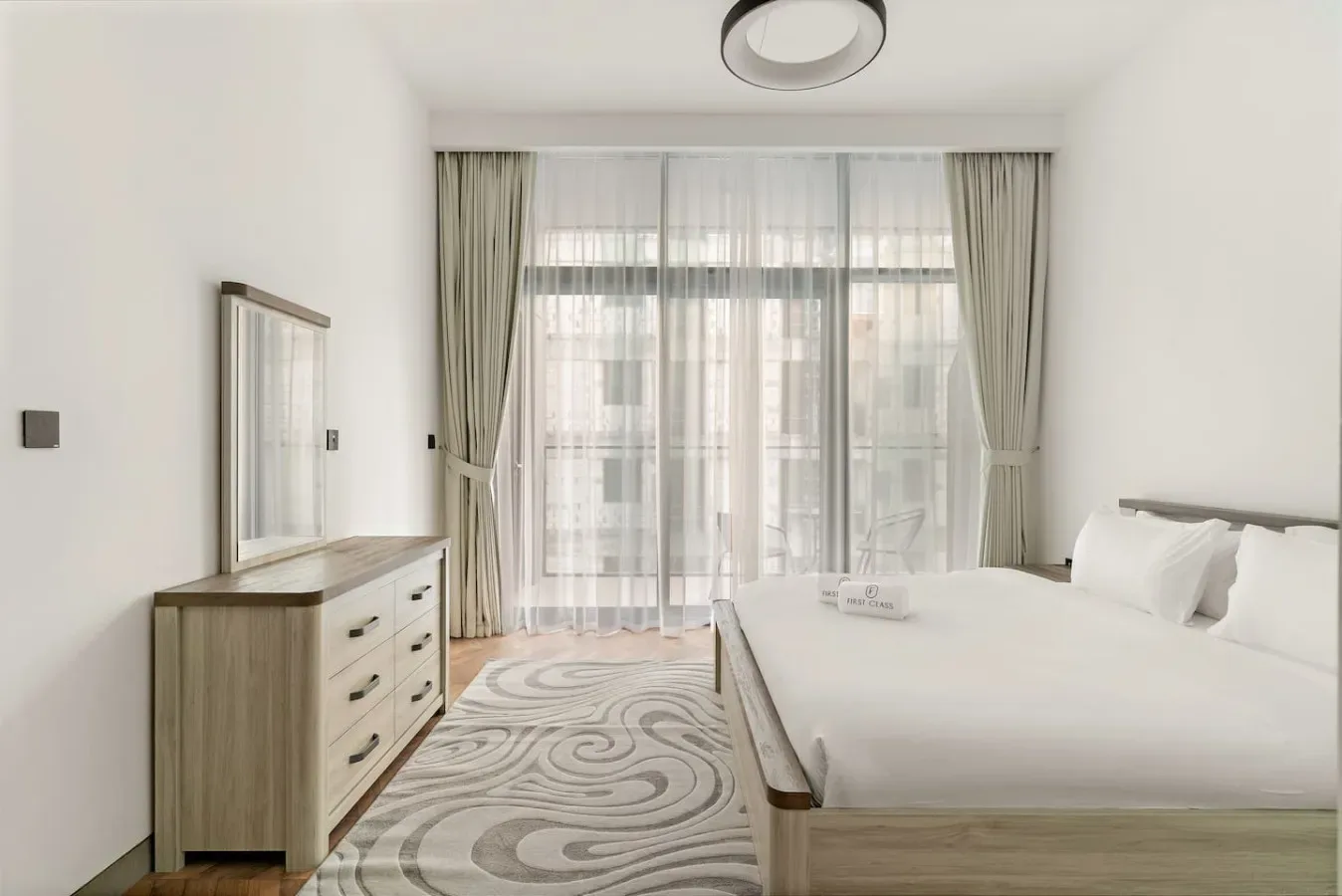 Un dormitorio luminoso con una cama grande, una cómoda y una ventana con cortinas.