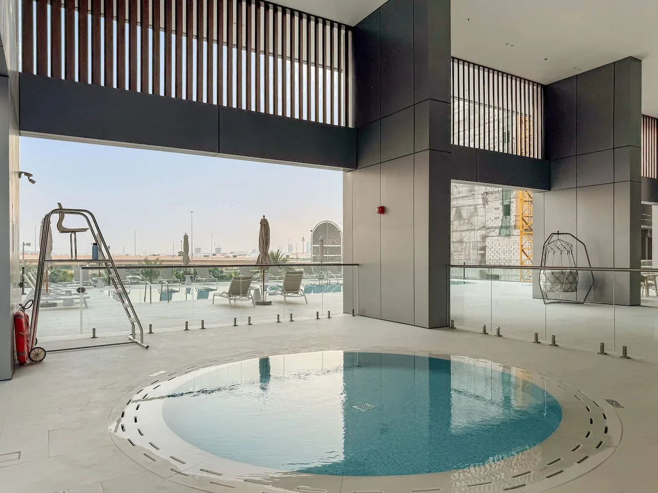 Una piscina cubierta está junto a ventanales con vistas a una terraza exterior.