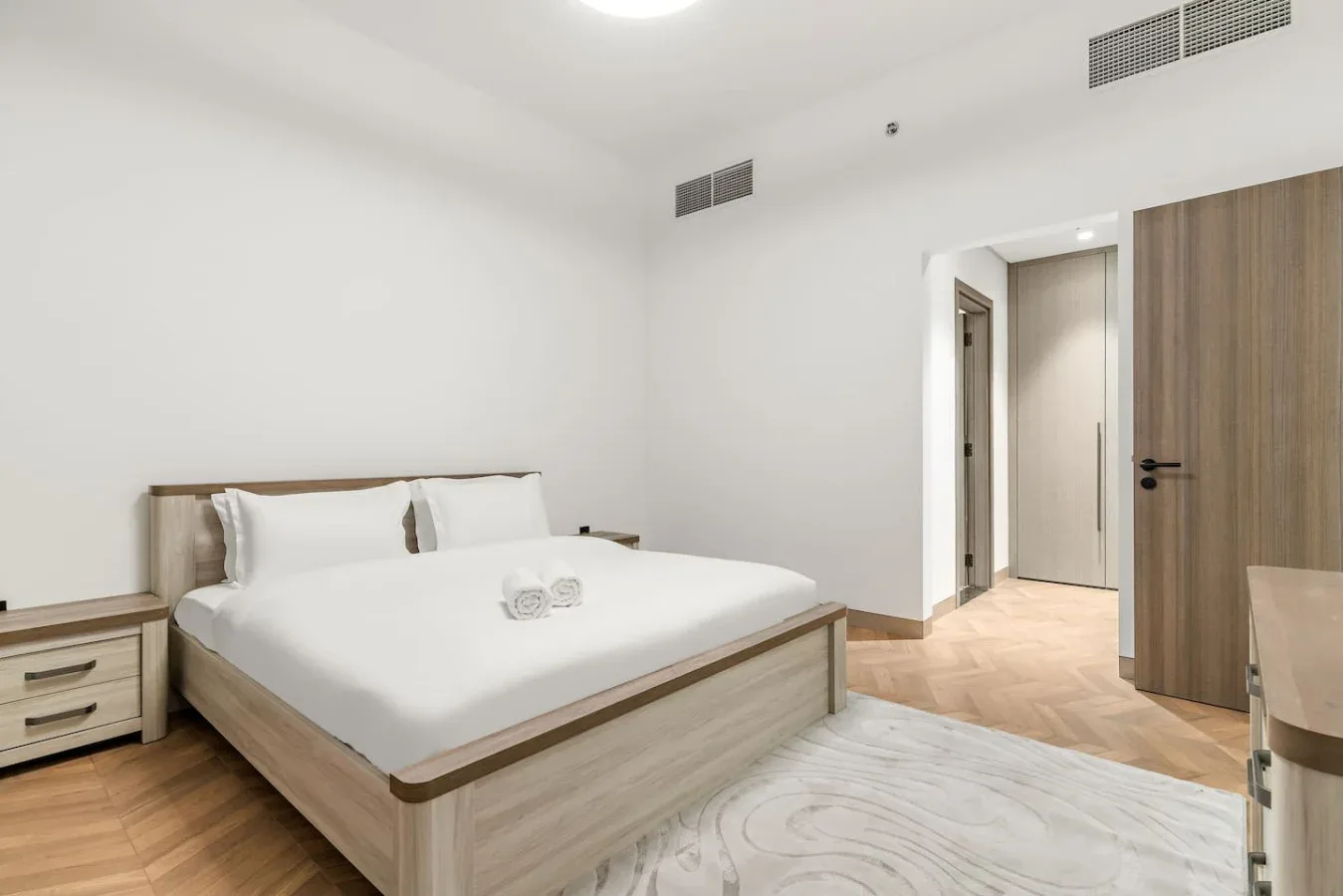 Un dormitorio luminoso con una cama bien tendida y muebles de madera clara.