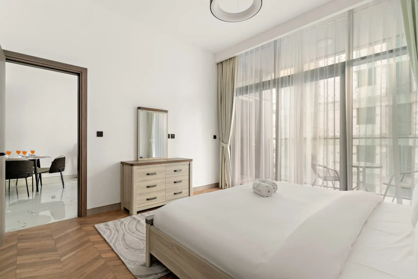 Un dormitorio luminoso con una cama junto a ventanales y cortinas translúcidas.