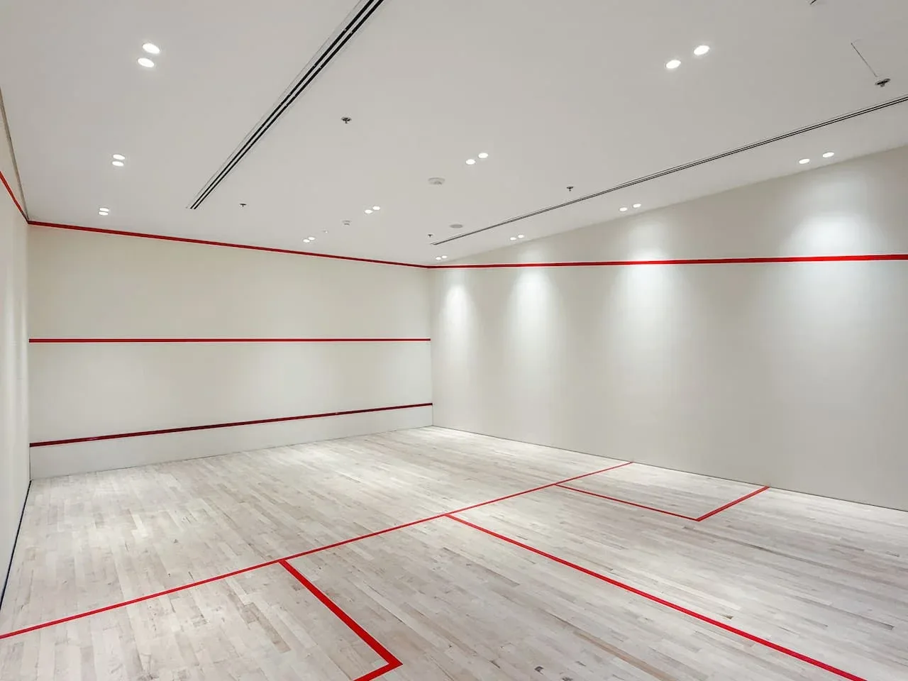 Una cancha interior vacía tiene líneas rojas sobre el suelo claro.
