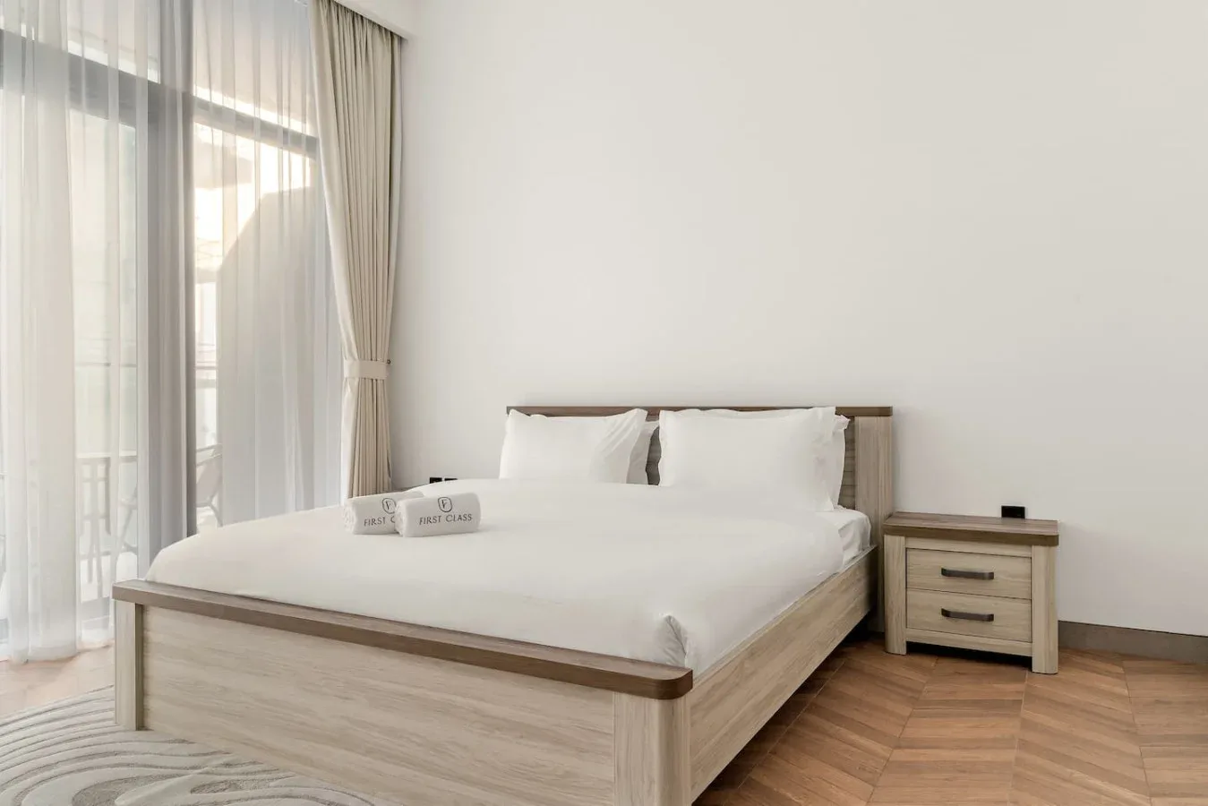 Un dormitorio luminoso con una cama bien tendida junto a una gran ventana con cortinas.