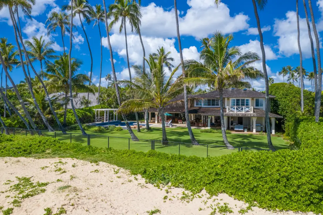Una casa tropical está rodeada de palmeras junto a una playa de arena.