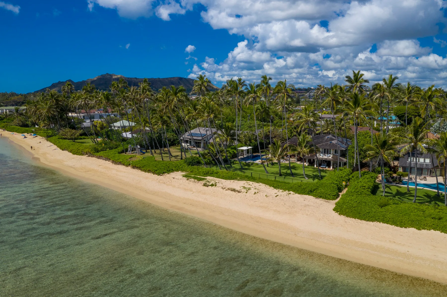 Vista aérea de una playa de arena junto a palmeras y edificios dispersos.