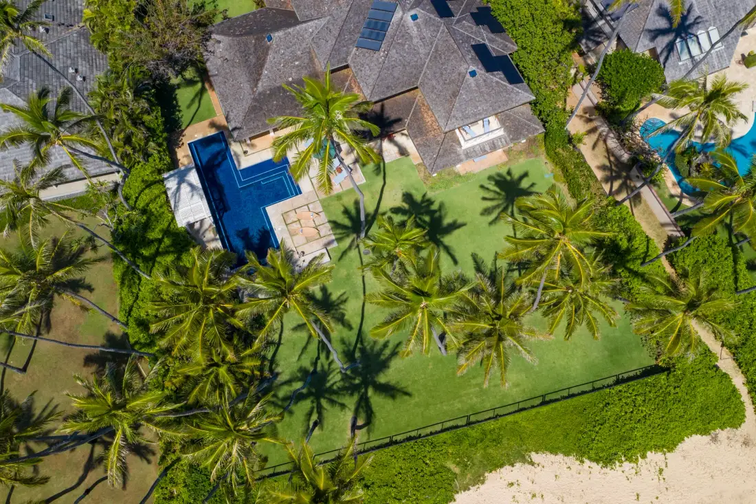 Vista aérea de un complejo tropical con edificios, palmeras y piscinas.