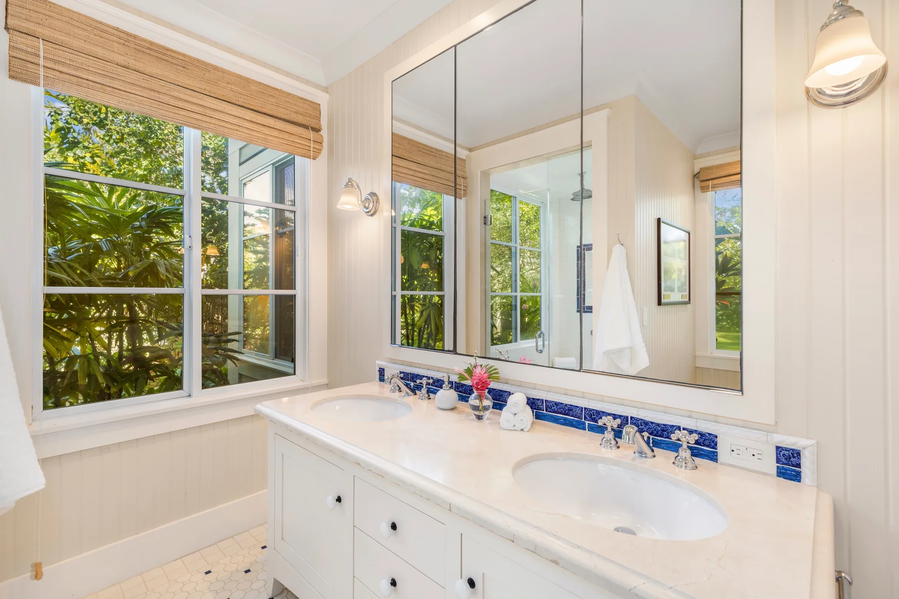 Un tocador de baño luminoso con un espejo grande y vistas de hojas verdes por las ventanas.