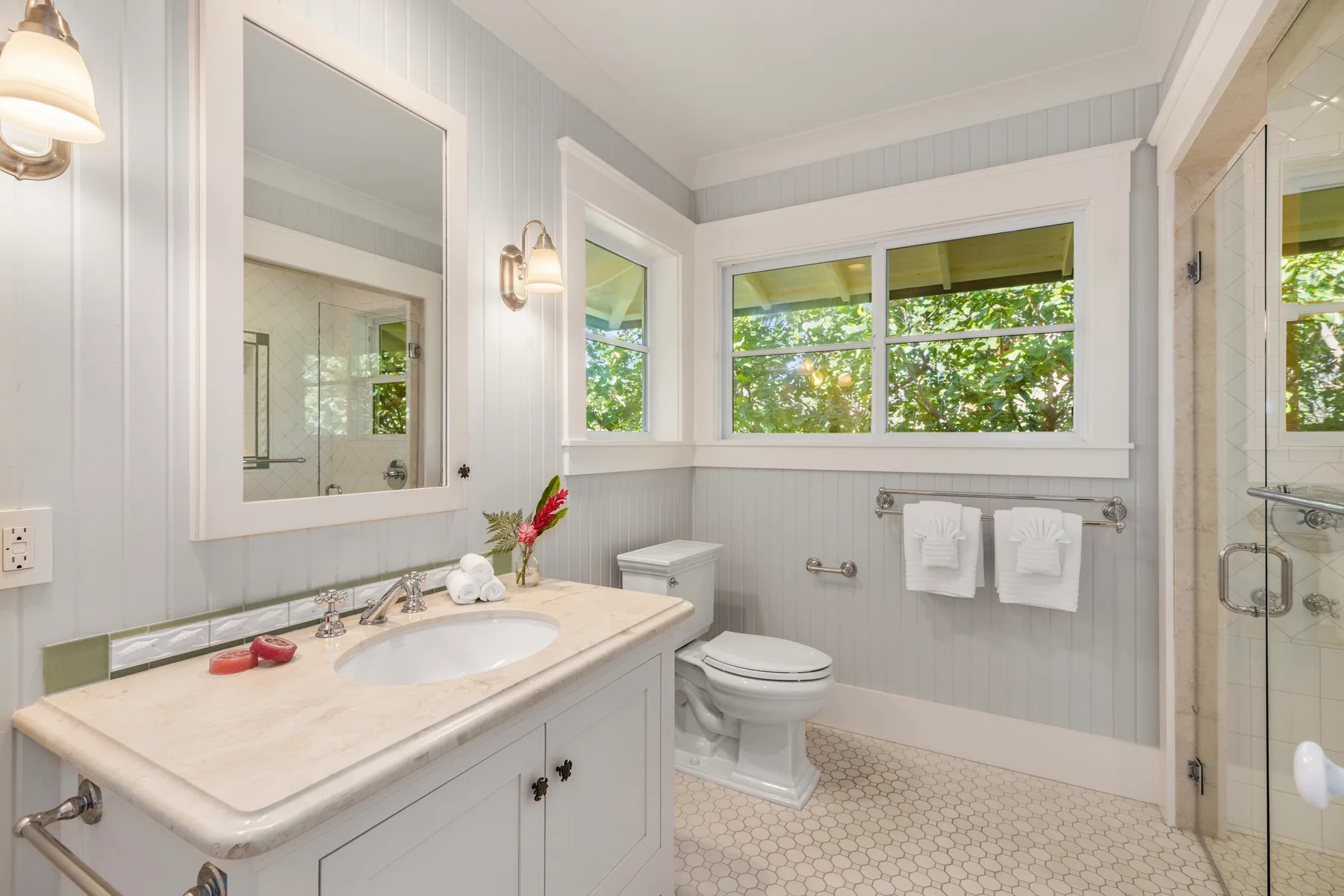 Un baño luminoso con un tocador largo, inodoro y ventanas con vistas a la vegetación.