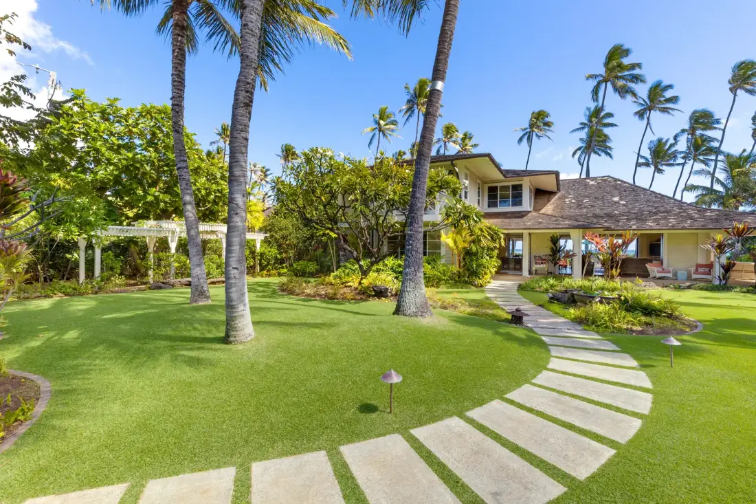 Un jardín tropical ajardinado con palmeras y un sendero curvo de piedra.