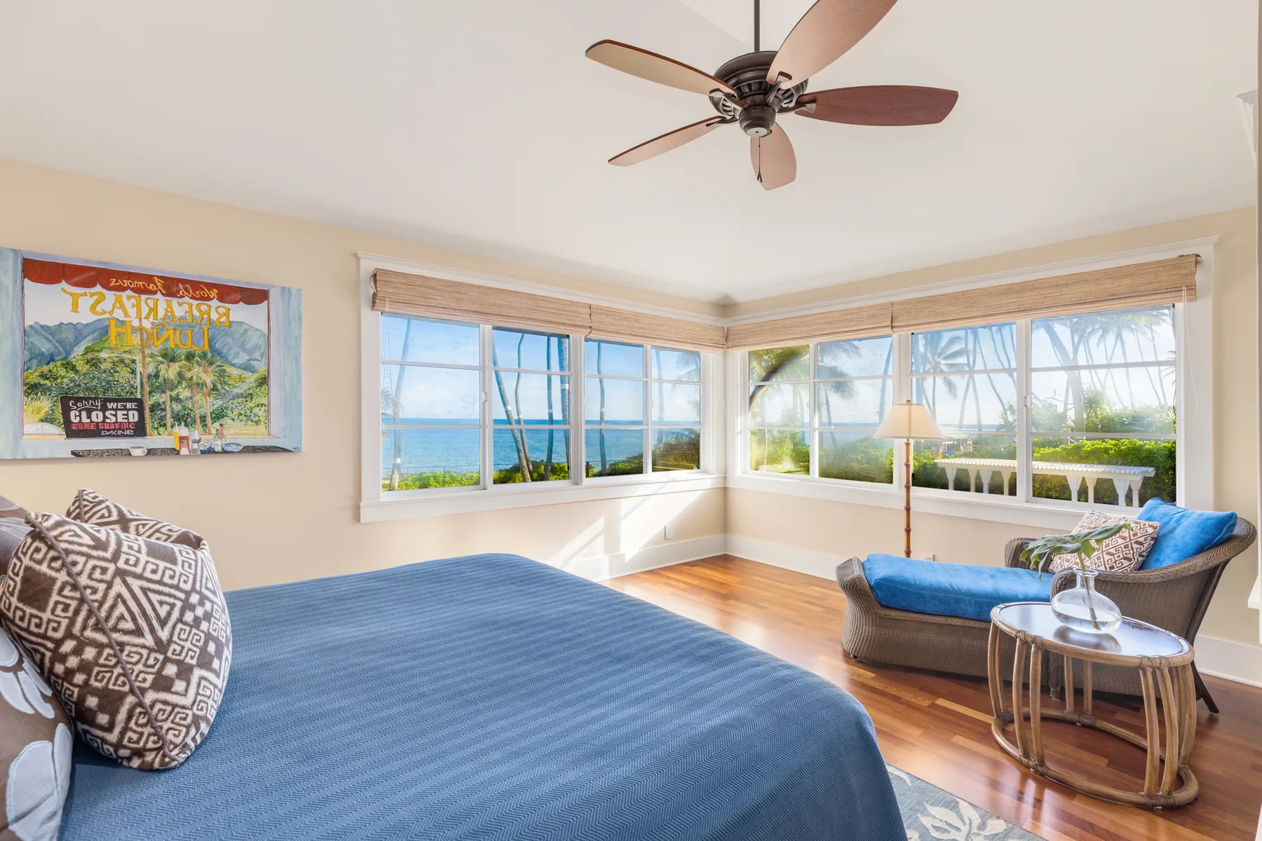 Un dormitorio con una cama, un ventilador de techo y grandes ventanas con vista al agua.