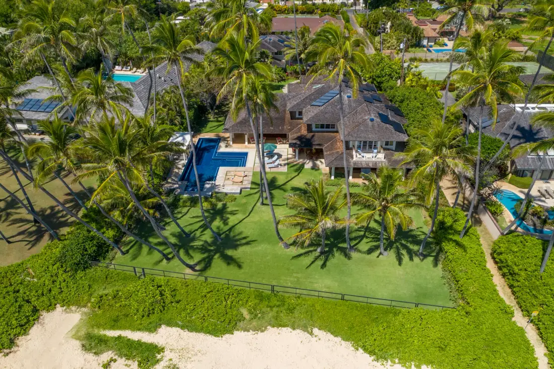 Vista aérea de una propiedad junto a la playa, con piscina y palmeras.