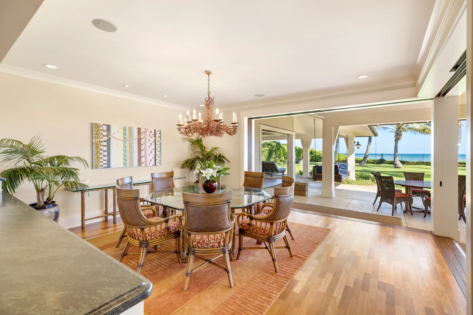 A dining area opens onto a patio and ocean view through wide glass doors.