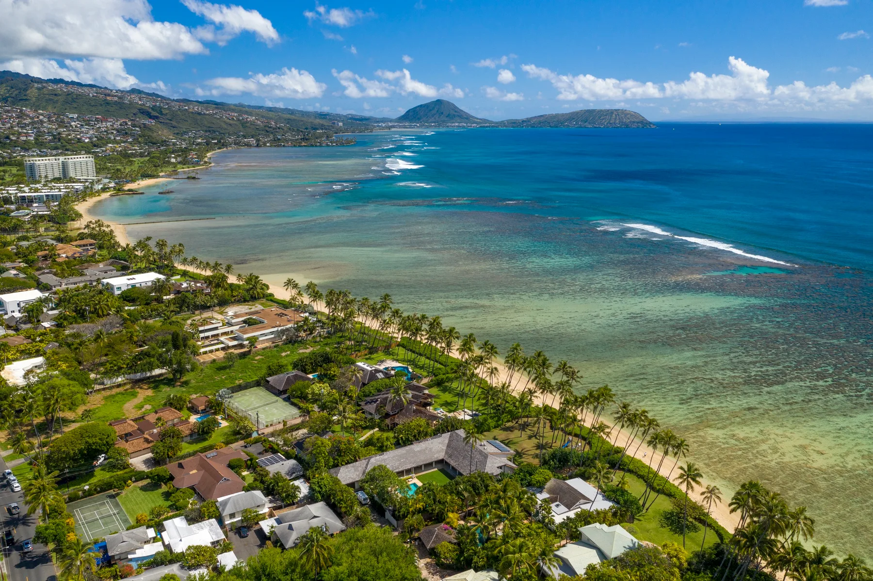 Vista aérea de una costa tropical con aguas turquesas y casas junto a la playa.