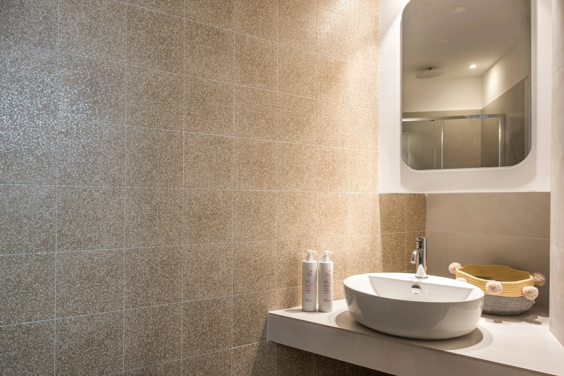 Un lavabo de baño alicatado con un lavabo blanco y un espejo de pared.