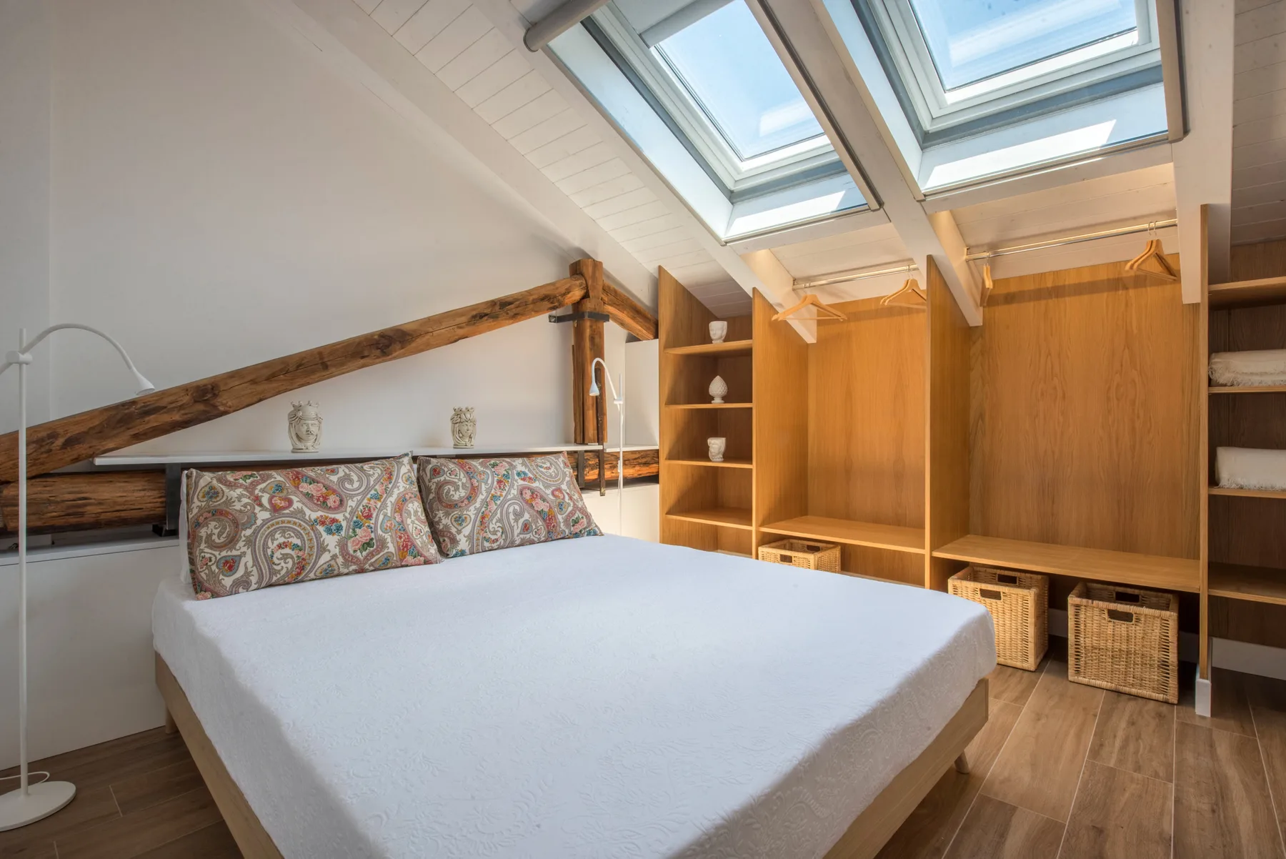 Un dormitorio con una cama bajo tragaluces y armarios de madera.