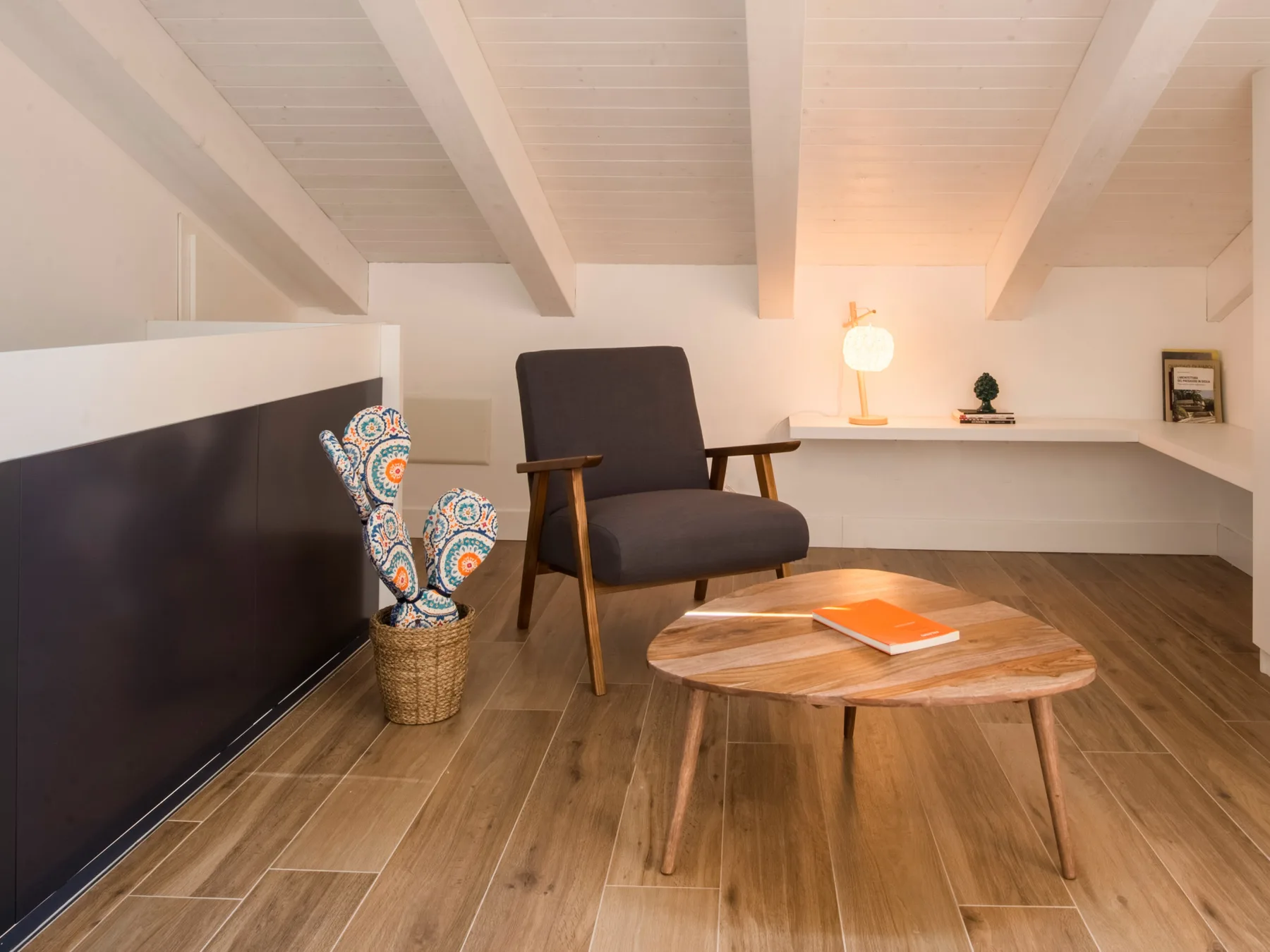 Una zona de estar en un altillo tiene un sillón oscuro, una mesa baja y un televisor.