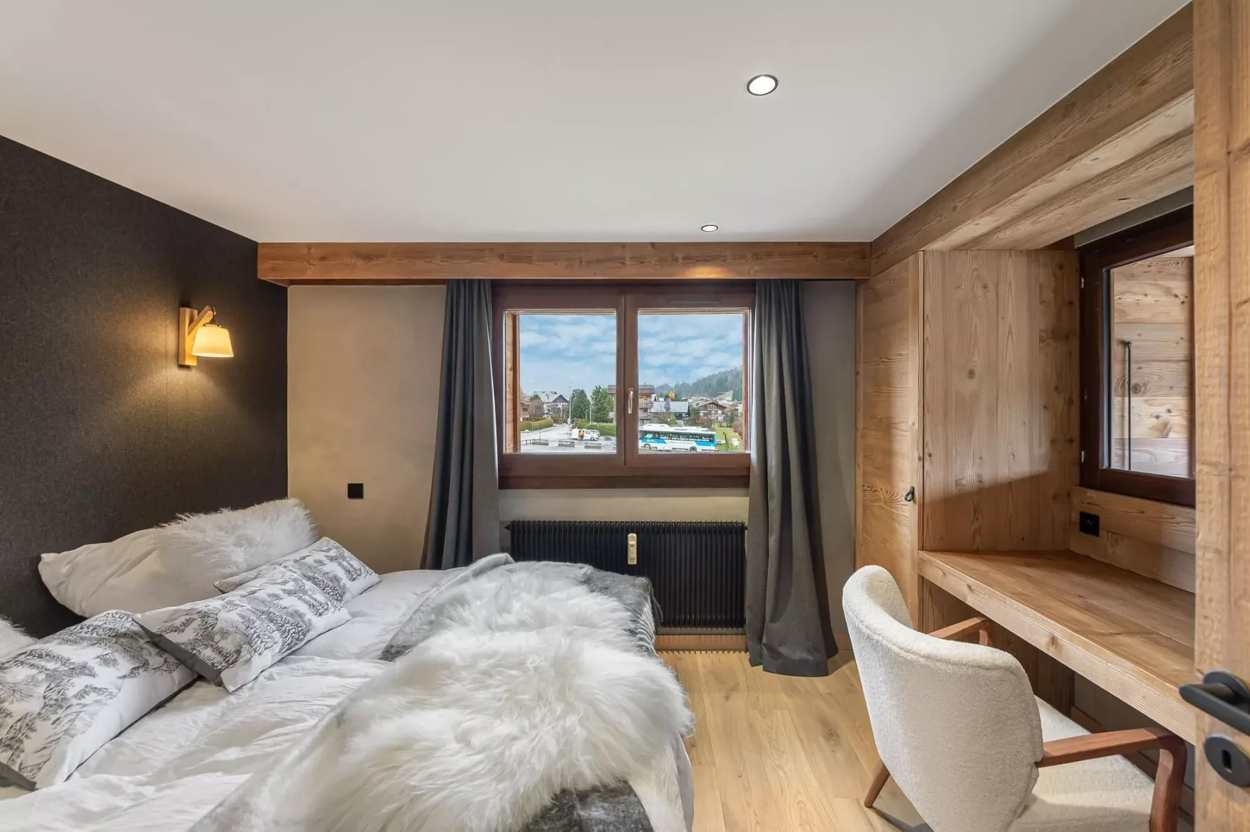 Un dormitorio con un escritorio junto a la ventana y vistas a un pueblo de montaña.