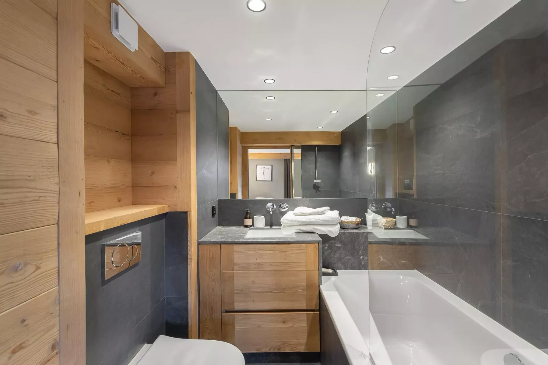 Un baño moderno con bañera, ducha de cristal y muebles de madera.