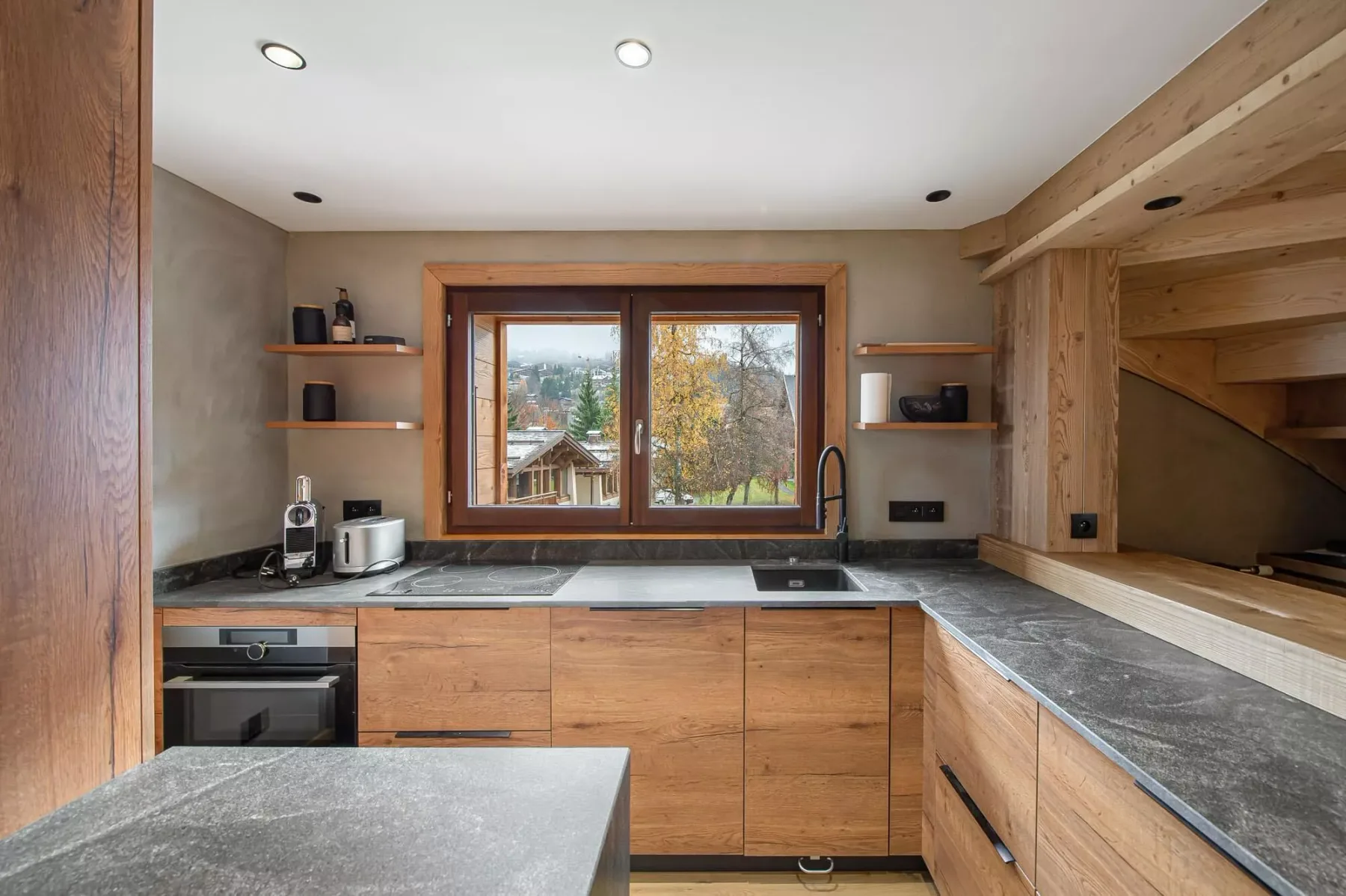 Una cocina con acabados de madera y una gran ventana sobre la encimera.