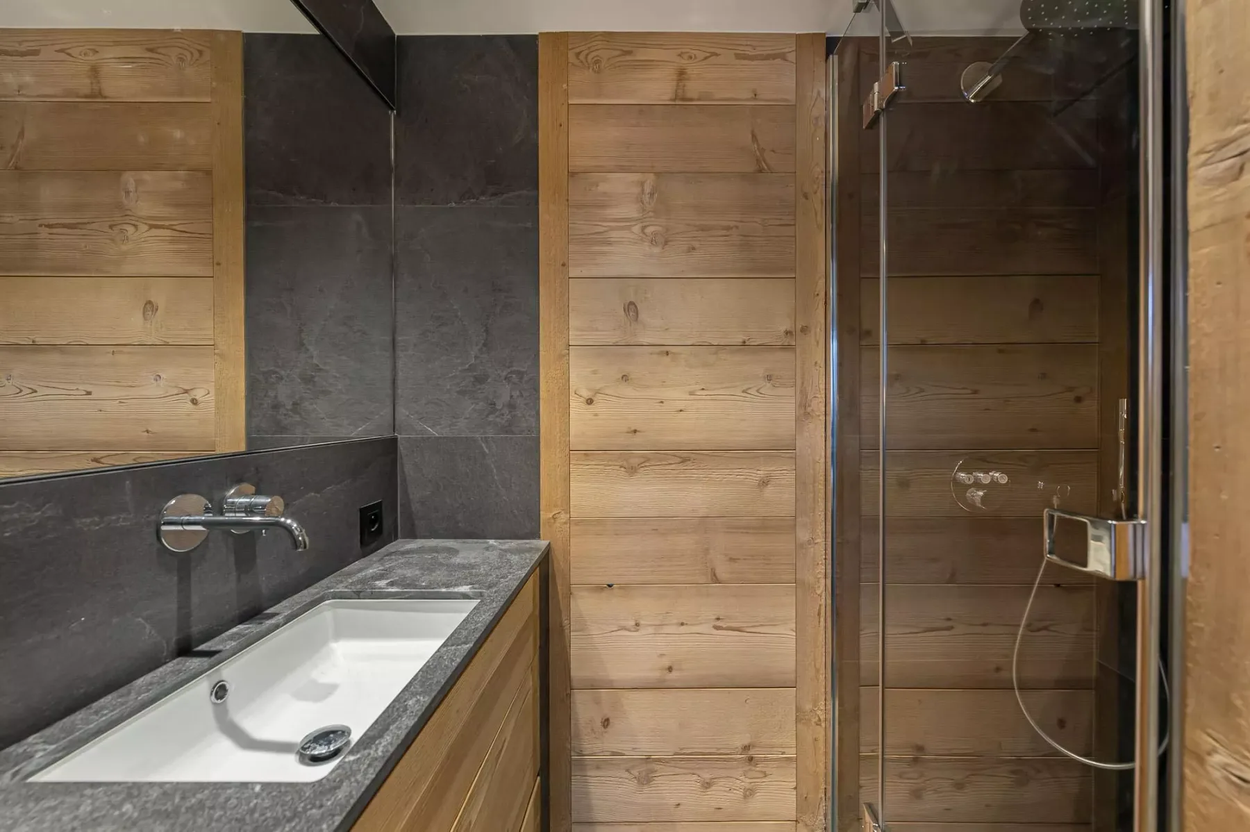 Un baño con una encimera larga con lavabo junto a una ducha de vidrio.