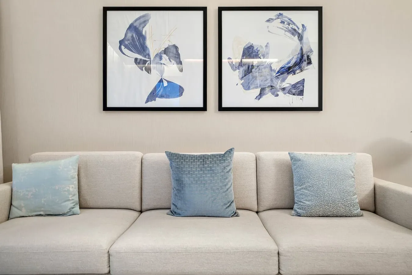Una zona de estar clara con cojines azules y obras abstractas enmarcadas.