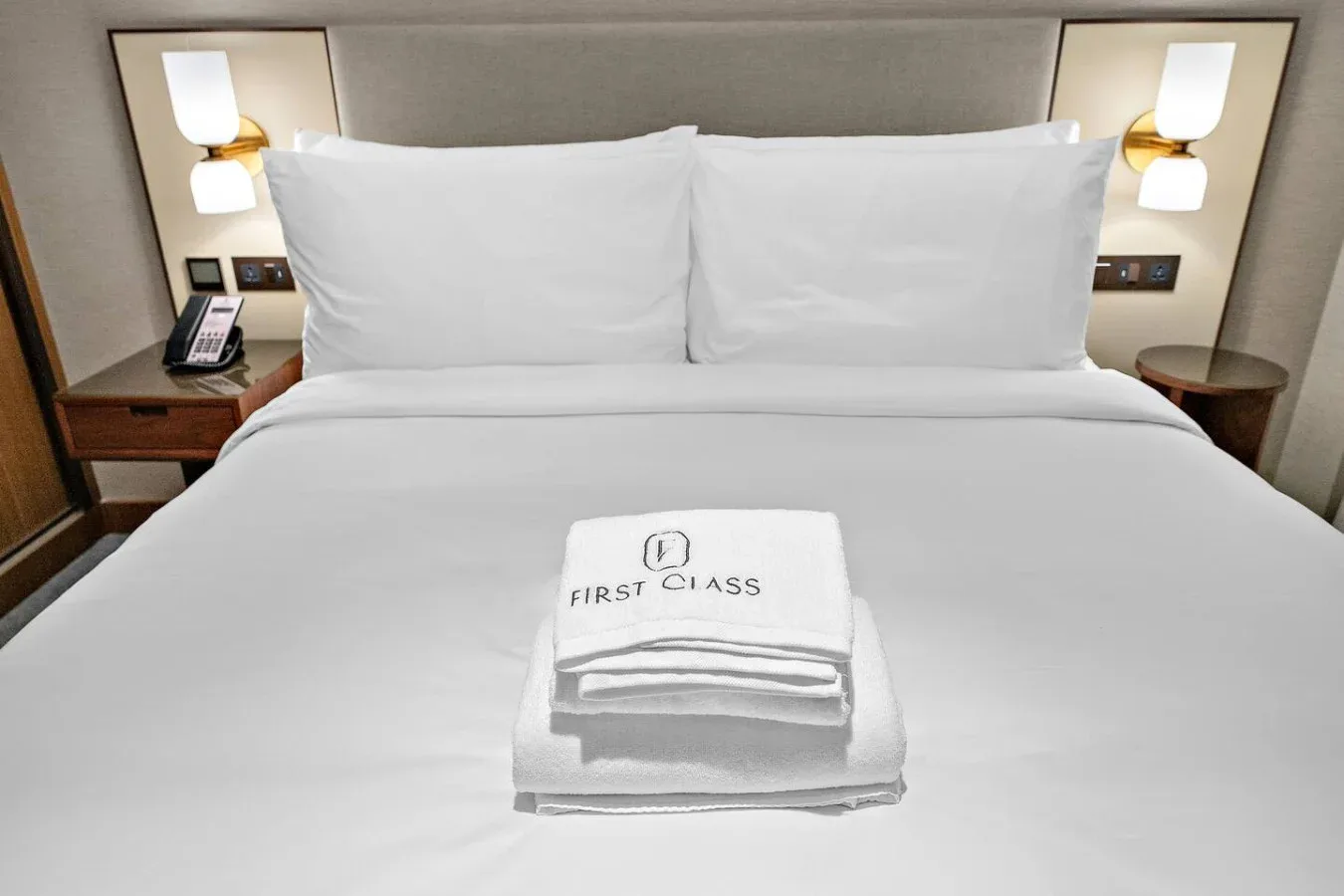 Una cama bien tendida con ropa de cama blanca y toallas dobladas.