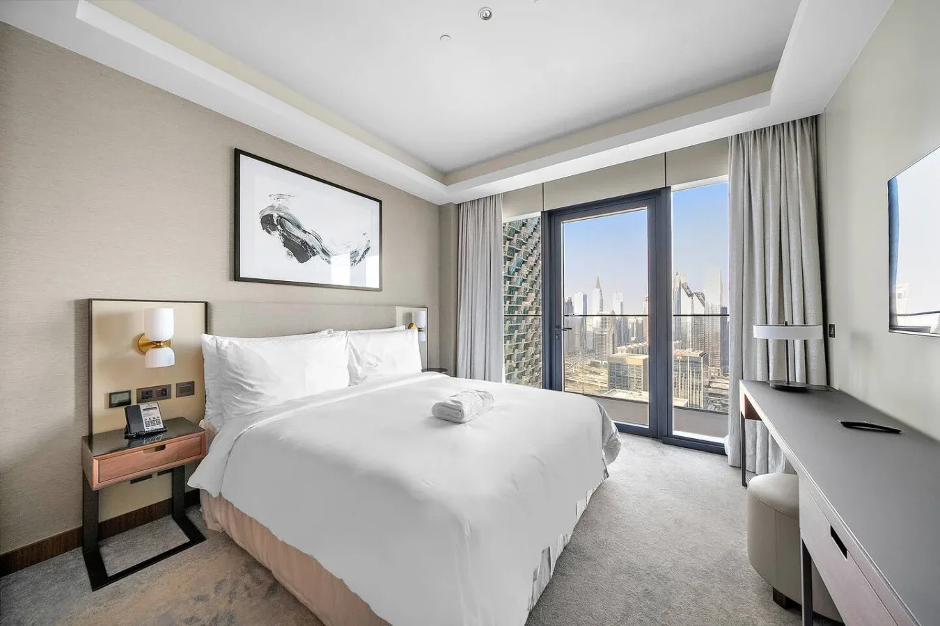 Un dormitorio luminoso con una cama bien tendida y grandes ventanas con vistas a la ciudad.