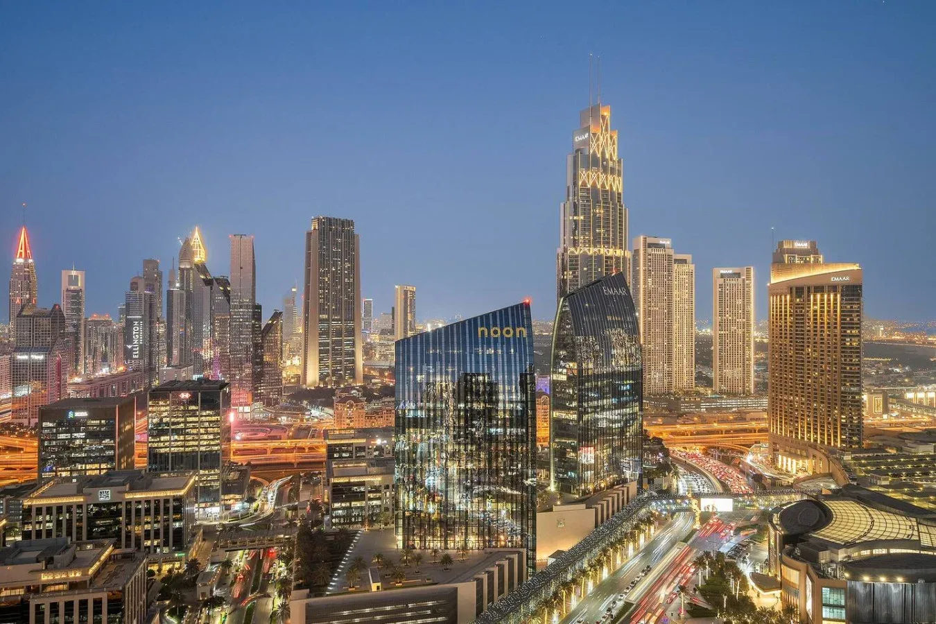 Panorámica urbana al anochecer, con edificios iluminados y tráfico abajo.