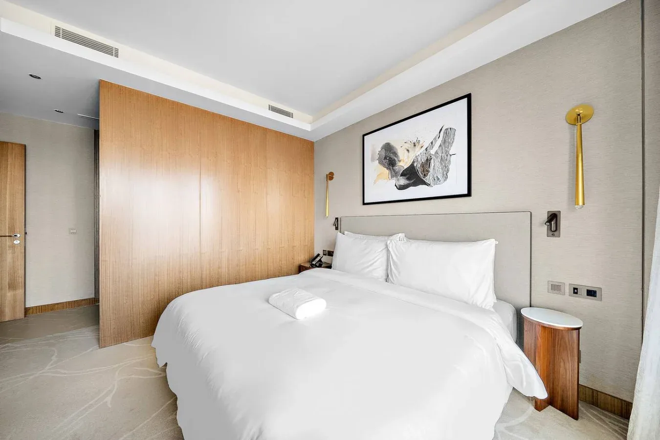 Dormitorio con una cama bien tendida y una obra enmarcada sobre el cabecero.