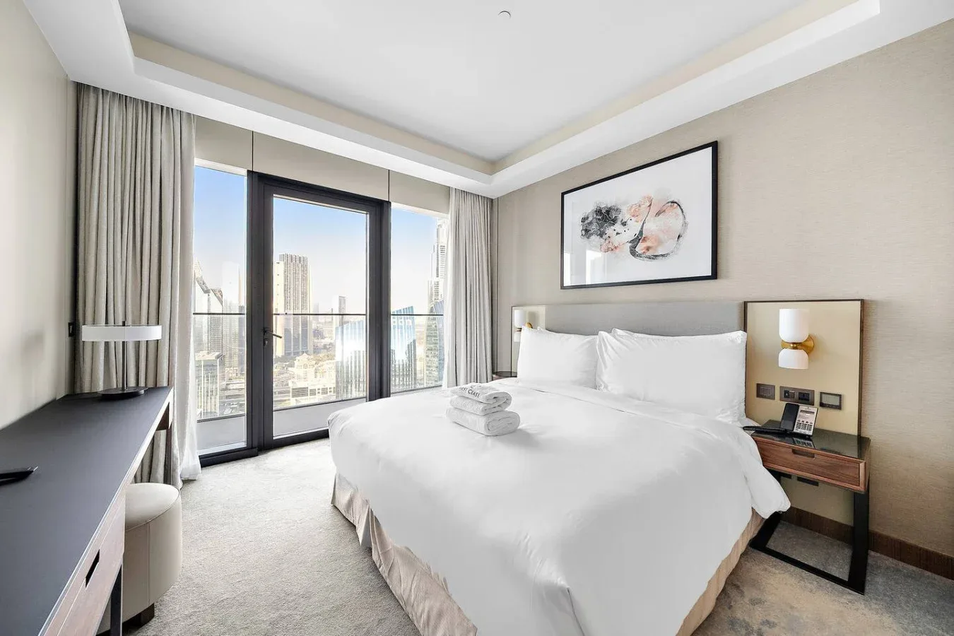 Un dormitorio luminoso con una cama tendida junto a ventanales de piso a techo.