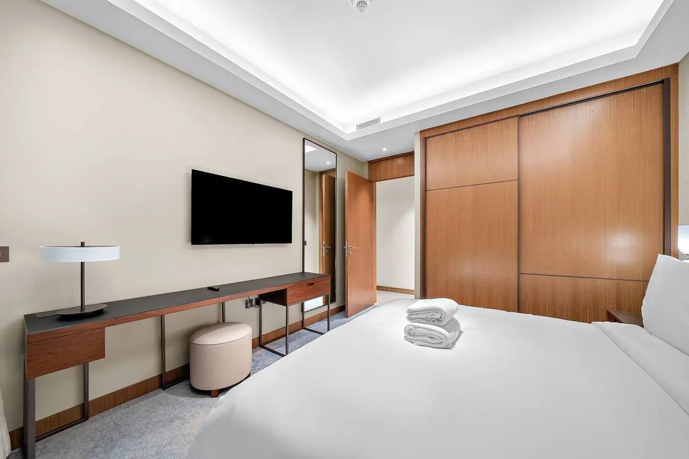 Dormitorio con cama, televisor montado en la pared y puertas de armario de madera.