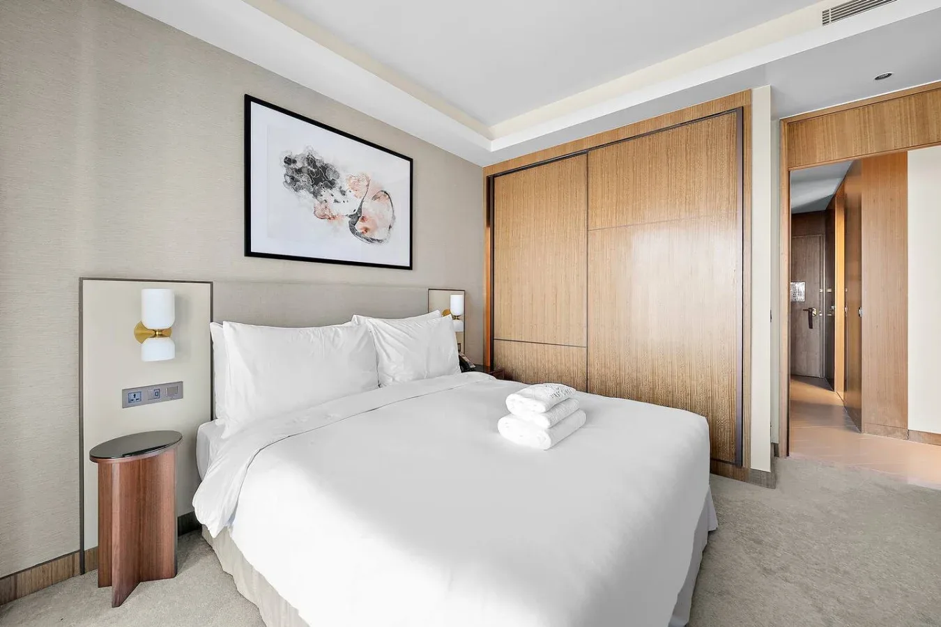 Un dormitorio con una cama bien tendida, toallas dobladas y una obra enmarcada.