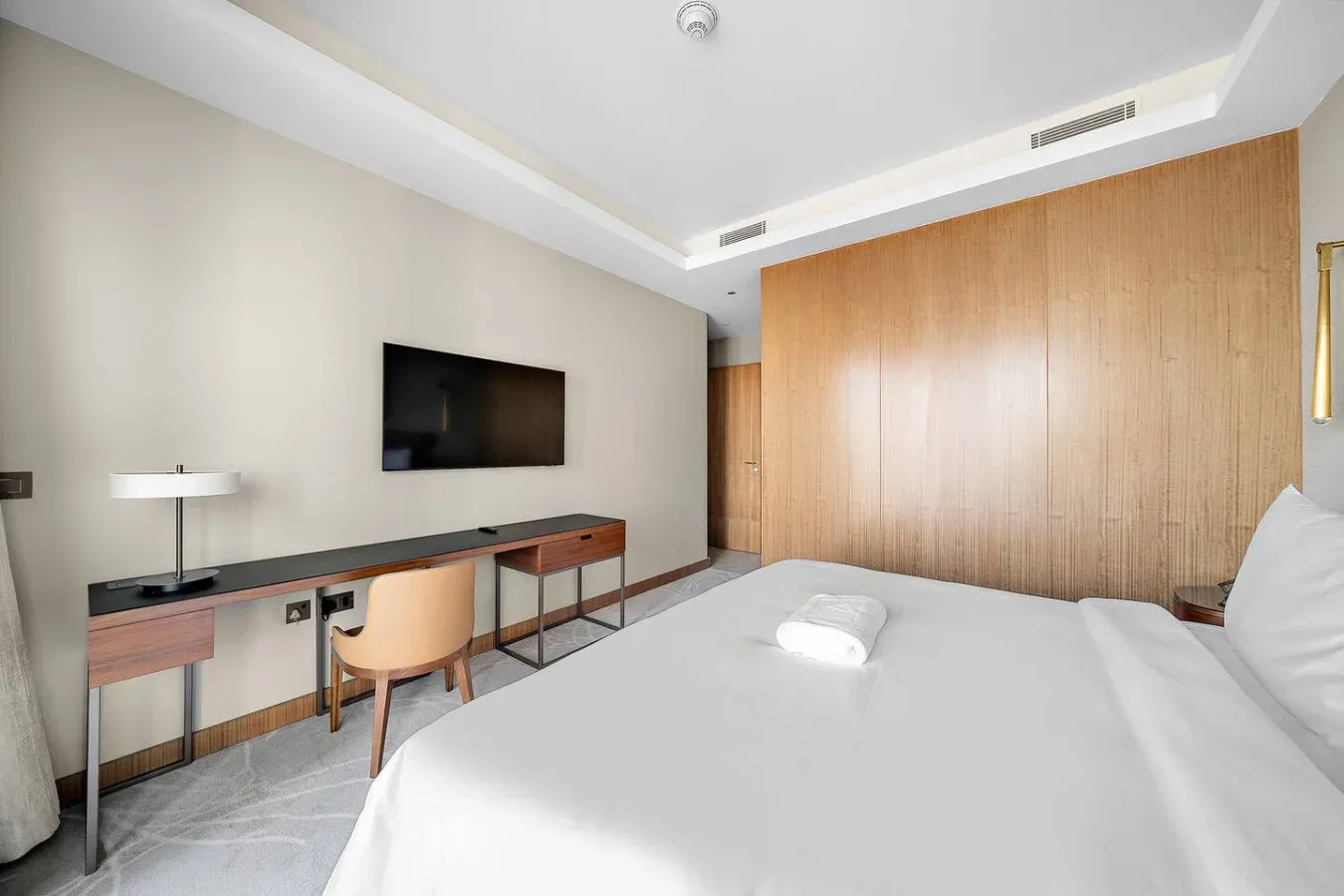 Un dormitorio con una cama, un televisor montado en la pared y un escritorio junto a la pared.