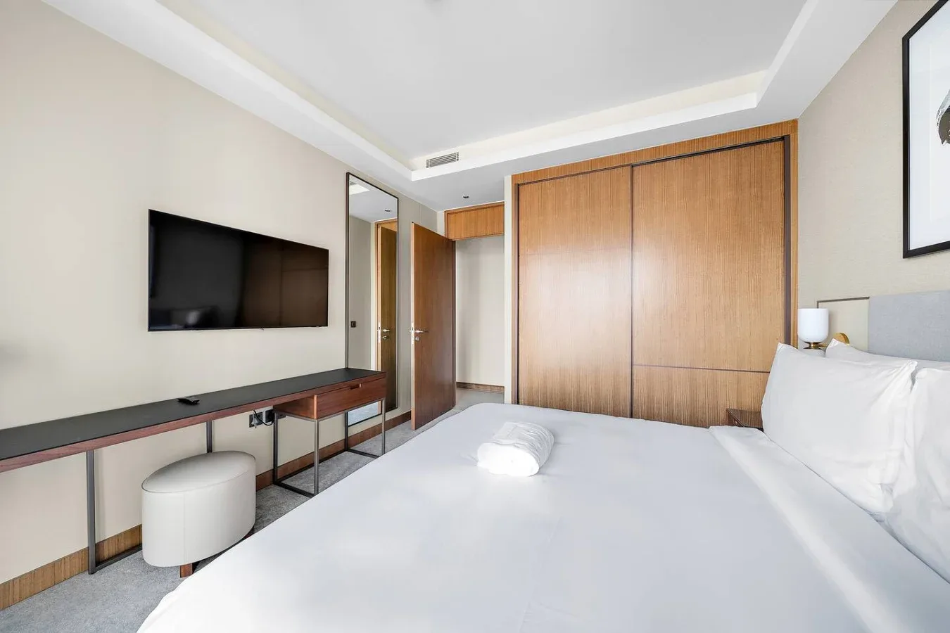 Un dormitorio luminoso con una cama grande, un televisor montado en la pared y puertas de armario de madera.