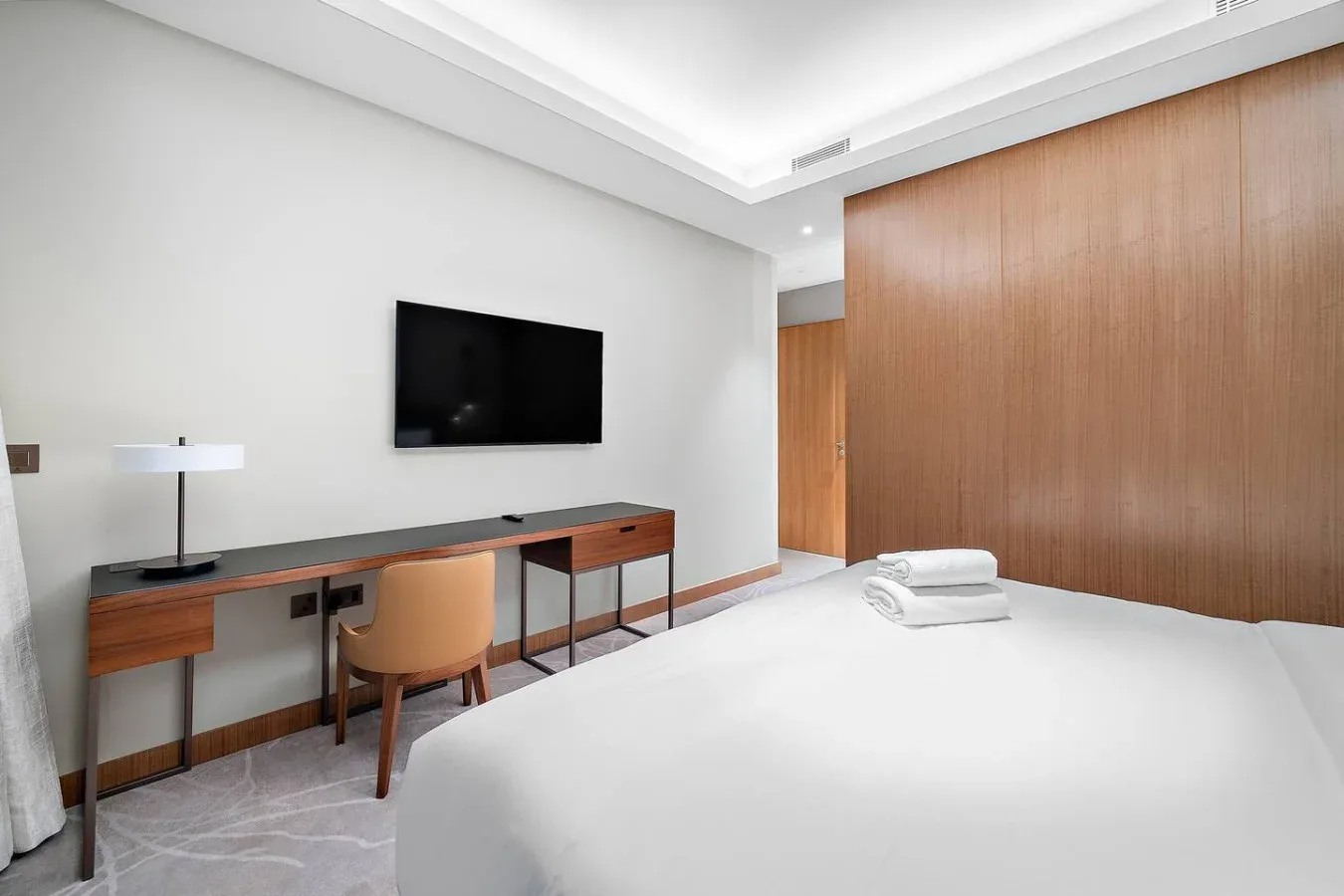 Un dormitorio con cama, escritorio, silla y televisor montado en la pared.