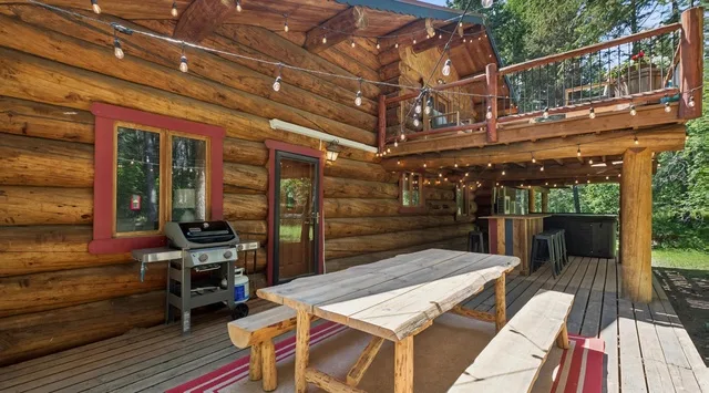 Una terraza de madera con una mesa de pícnic, una parrilla y un balcón arriba.