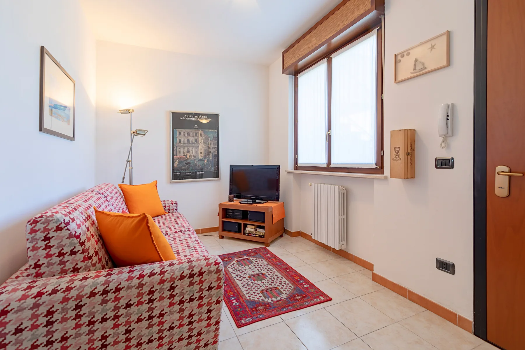 Una sala de estar con asientos estampados, un televisor y una ventana grande.