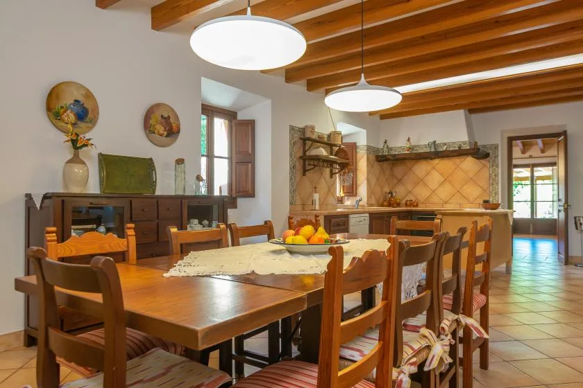 A dining area with a long wooden table and chairs beneath exposed ceiling beams.