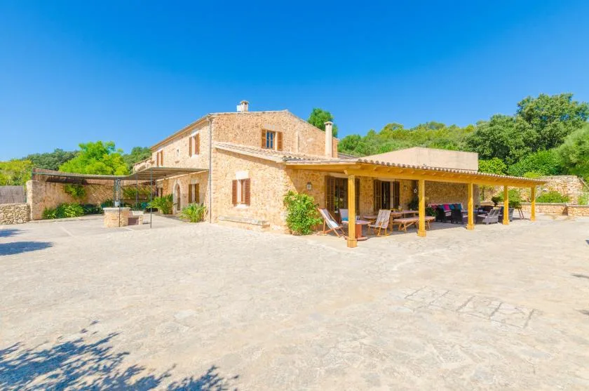 A stone house with a covered patio opens onto a wide paved courtyard.