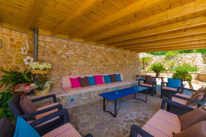 A covered stone patio with cushioned seating and a blue table.