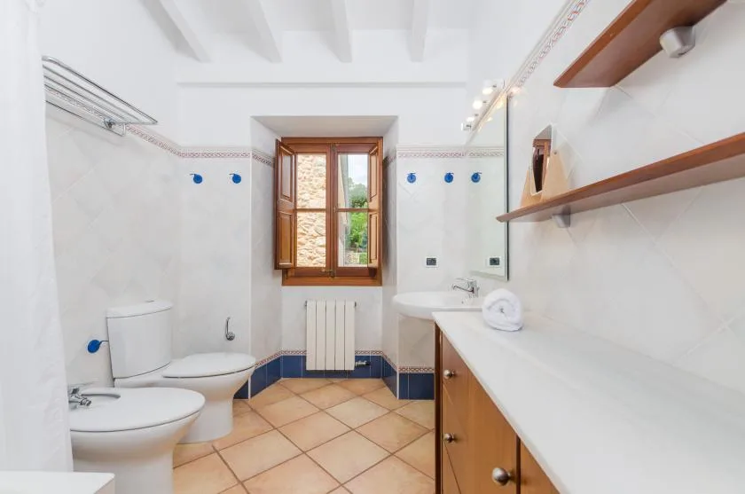A tiled bathroom with a window, sink, and toilet.