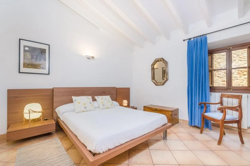 A bright bedroom with a bed, bedside tables, and a window with blue curtains.