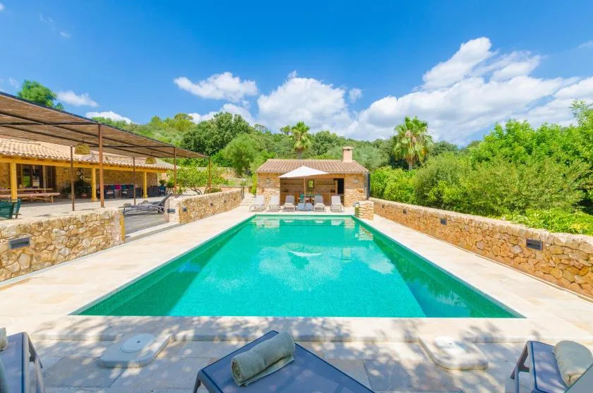 A turquoise swimming pool sits beside stone walls, with a covered patio beyond.