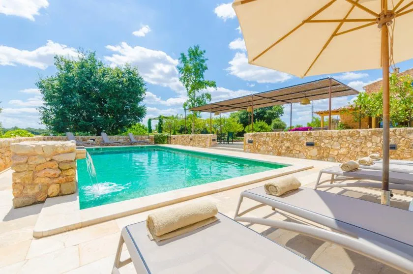 An outdoor swimming pool with cushioned loungers and a large sun umbrella.