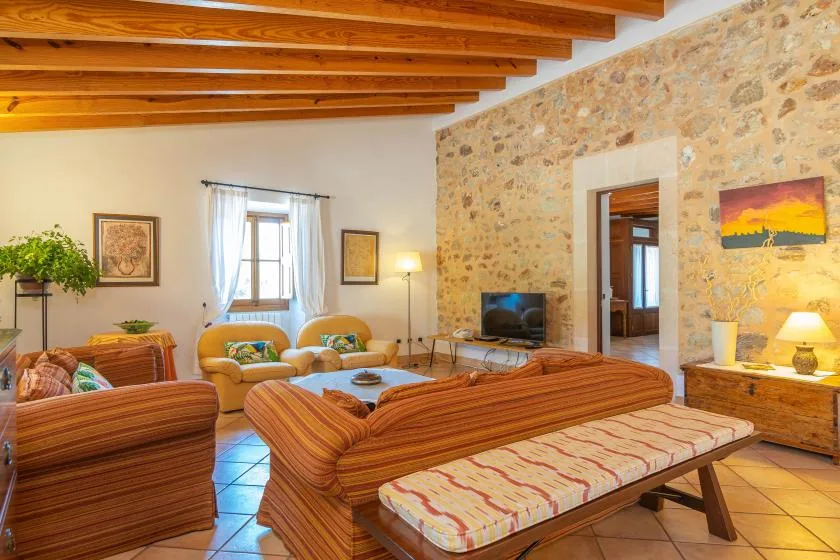 A warm living room with striped seating, exposed wooden beams, and a stone wall.