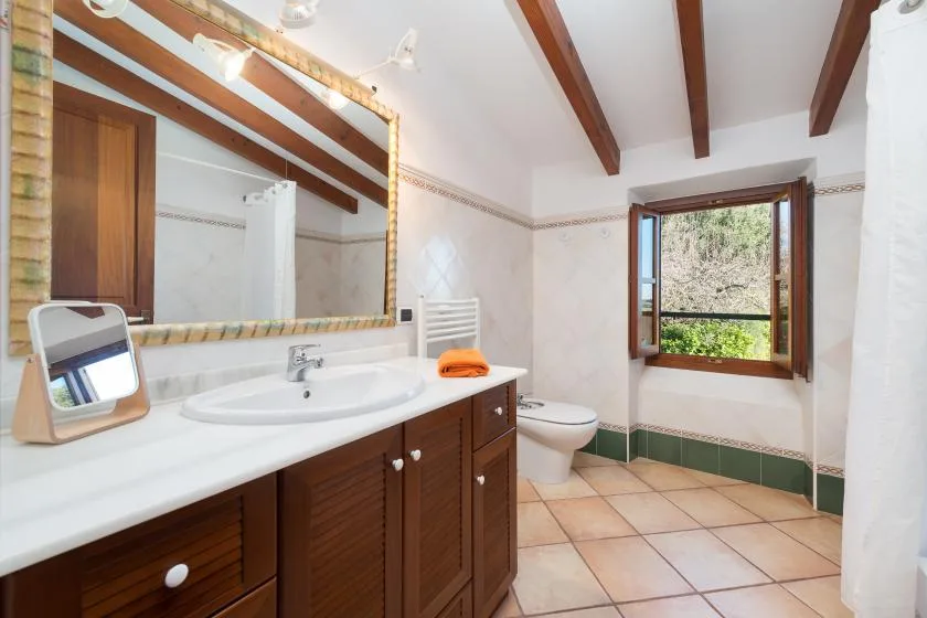 A tiled bathroom has a long vanity, a toilet, and a window.