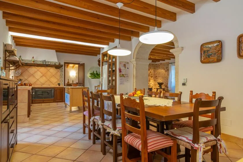 A dining area with a long wooden table and chairs beneath exposed ceiling beams.