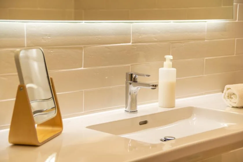 A bathroom sink with a chrome faucet and countertop mirror.